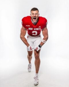 JAX State football player in a red jersey (#3) sprinting forward and shouting toward the camera on a white studio background.",
